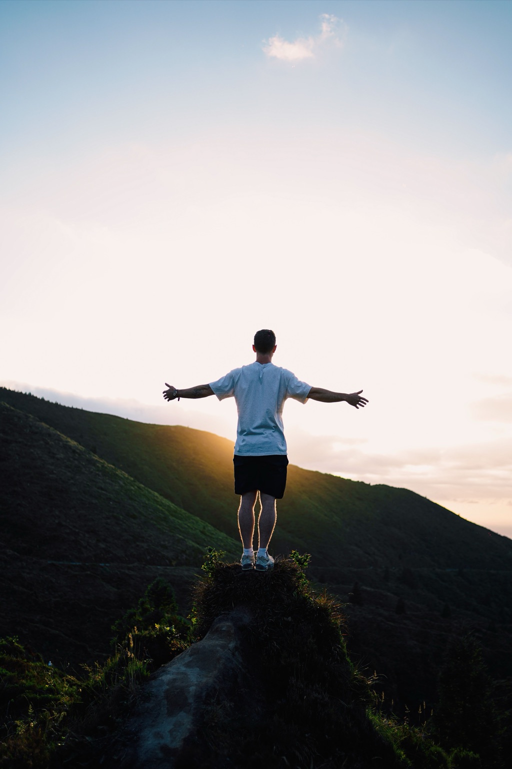 A man stands on a hilltop at sunrise with his arms open wide