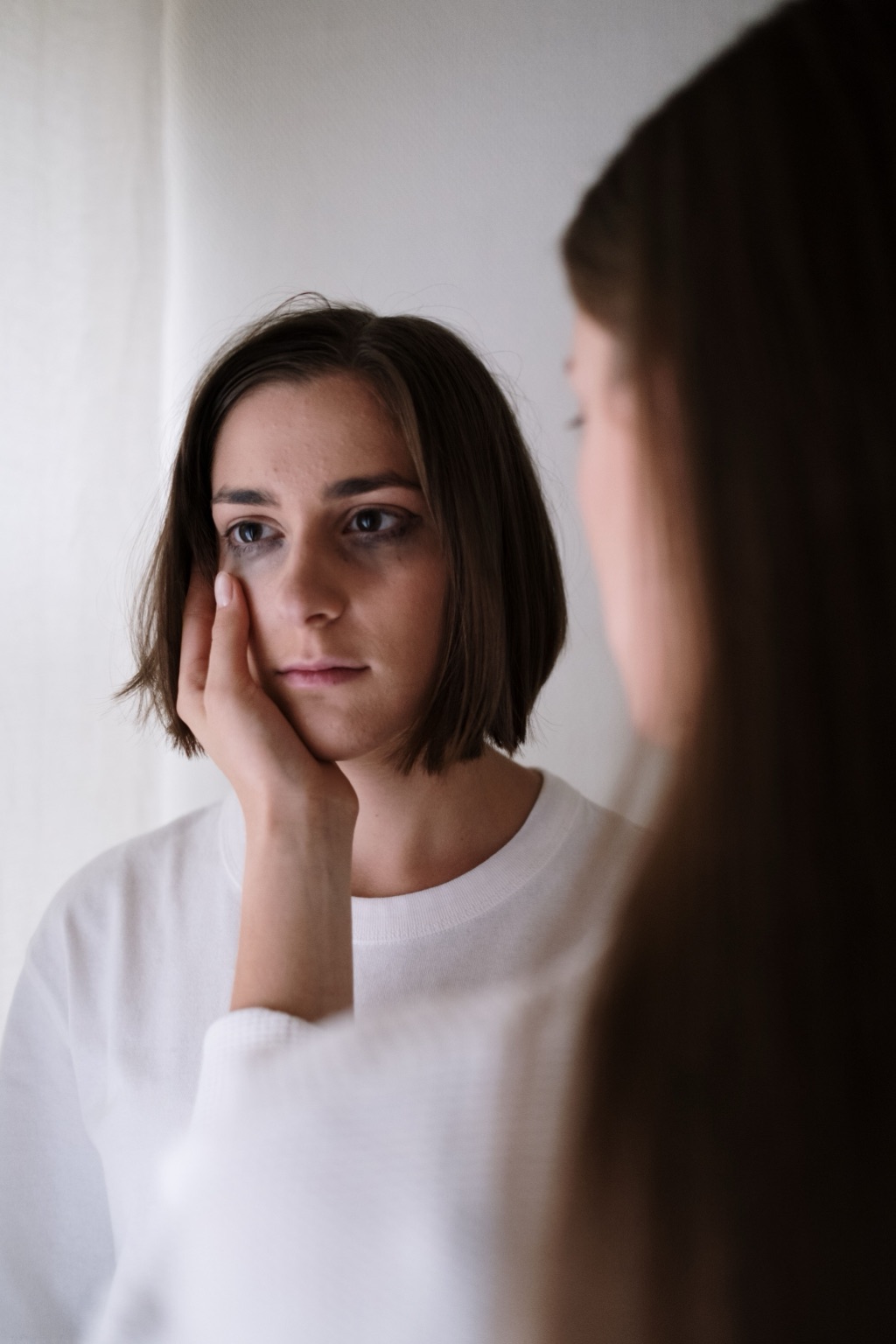 A woman looks thoughtfully at her reflection in a mirror