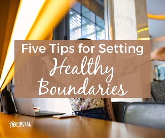 tan box with text that reads "Five tips for setting healthy boundaries" over a photo of a middle-eastern woman sitting at her desk in front of an open laptop, stretching her arms and smiling.