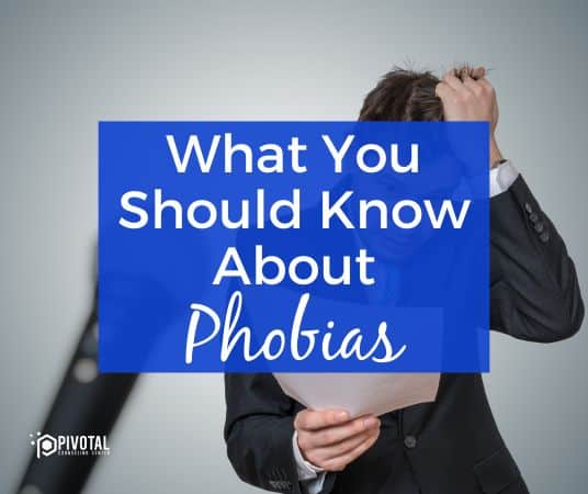 A distressed man in a suit grabbing at his hair and looking down at a paper in his hand and a microphone slightly out of focus against a gray background and a blue box that reads "What you should know about Phobias"