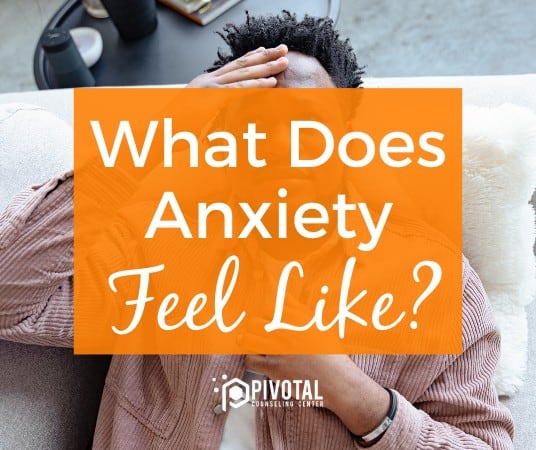 African American man touching his forehead with his right hand behind an orange box that reads "what does anxiety feel like"