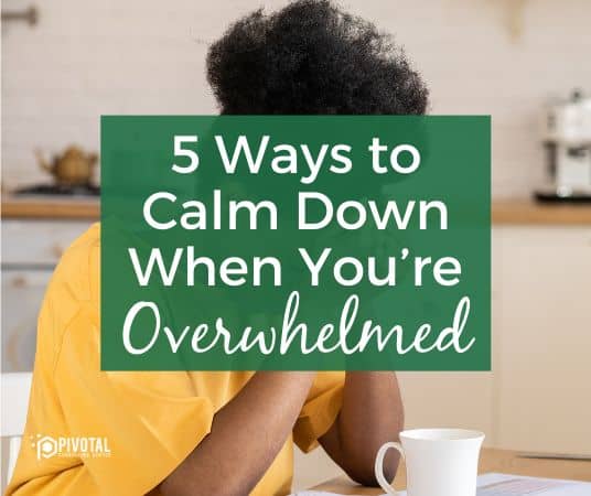 A graphic that reads "5 Ways to Calm Down When You’re Overwhelmed" in white text on a dark green text box overlaid on top of a stock photo of a Black woman sitting at a table with her head in her hands and a coffee cup and papers spread out in front of her.